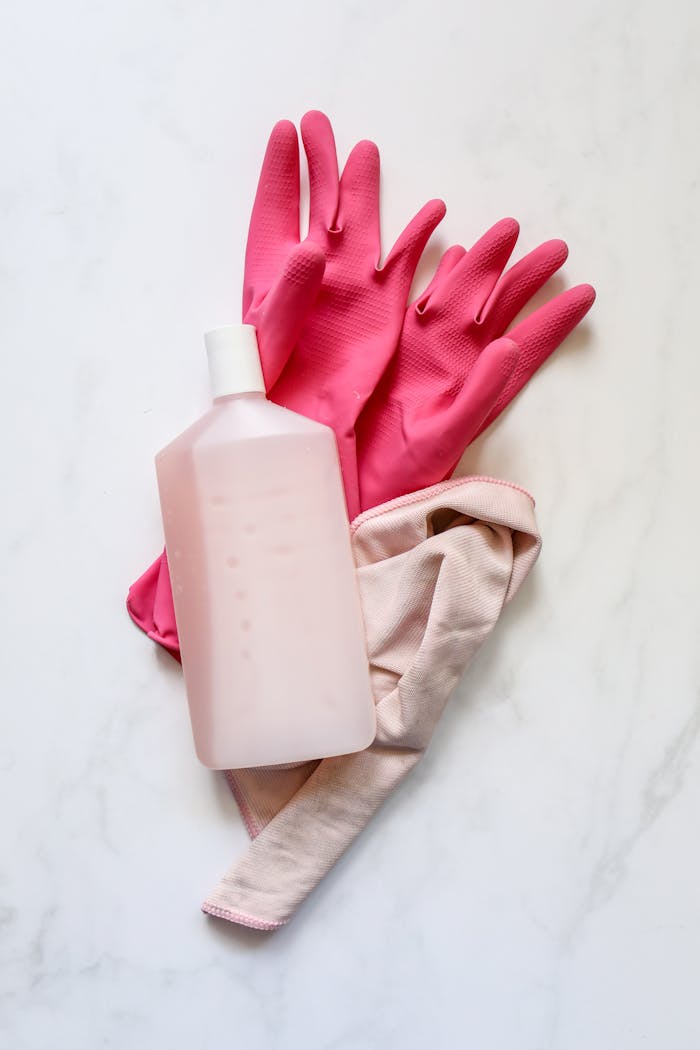 our-story A flat lay of pink rubber gloves, a cleaning cloth, and a bottle on a white background for cleaning themes.